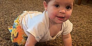 Mila is registered to the contest to win money with this photo: baby, carpet, carpet_texture, child, colorful_pants, crawling, curious, floor, furniture, happy, home, indoors, living_room, person, smiling, sunflower_pattern, television, white_shirt, wooden_chair, young_child