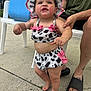 adult_hand, barefoot, casual, chair, child, concrete, cooler, cow_print, footwear, hat, outdoor, person, pink_bows, skin, smiling, summer, sunhat, supporting, swimsuit, toddler