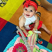 Mila joined the competition — help win amazing prizes! baby, child, headband, red, white_clothing, strawberry, play_mat, toy, colorful, smiling, indoor, floor, toddler, cute, happy, patterned, striped, sitting, person, playtime