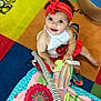 baby, child, headband, red, white_clothing, strawberry, play_mat, toy, colorful, smiling, indoor, floor, toddler, cute, happy, patterned, striped, sitting, person, playtime
