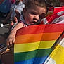background, beard, bracelet, building, child, clothing, colorful, crowd, event, face, festival, holding, outdoor, person, portrait, pride, rainbow_flag, sky, sunlight, toddler
