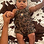 baby, child, infant, camo_overalls, blanket, cow_print, hand, holding, wide_eyes, expression, cute, lying_down, person, skin, face, fingers, legs, bed, comfort, soft