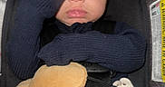 Zyon is registered to the contest to win money with this photo: baby, infant, car_seat, blue_clothing, mitten, plush_toy, pacifier, safety_harness, wide_eyes, face, hand, red_button, seatbelt, child, indoors, portrait, expression, closeup, person, cute