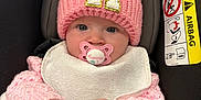 Harley Rose is registered to the contest to win money with this photo: baby, infant, pacifier, pink_hat, knitted_hat, pom_poms, blanket, car_seat, airbag_warning, clothing, cute, child, face, hands, warm, cozy, indoor, portrait, sitting, wrapped