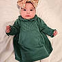 baby, infant, headband, bow, green_dress, knit_pattern, long_sleeves, tights, white_bedding, big_eyes, chubby_cheeks, portrait, hands, cute, indoor, soft_light, collar, lying_down, newborn, skin