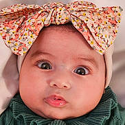 Layanah a rejoint le concours — aidez-le/la à gagner de superbes lots ! baby, infant, bow, headband, big_eyes, close_up, portrait, cute, lips, eyelashes, cheeks, skin, hat, floral_pattern, green_sweater, gaze, indoors, newborn, adorable, fashion