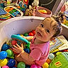 baby, child, ball_pit, colorful_balls, toy, pink_shirt, smiling, happy, indoor, playtime, topknot, book, reading, plastic_balls, cute, infant, playroom, childrens_toy, person, portrait