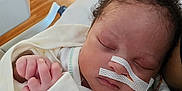 River is registered to the contest to win money with this photo: baby, sleeping, blanket, nasal_tube, hospital, medical_tape, person, hand, curly_hair, indoor, floor, clothing, resting, closeup, face, infant, newborn, comfort, hospital_bed, care