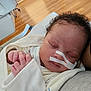 baby, sleeping, blanket, nasal_tube, hospital, medical_tape, person, hand, curly_hair, indoor, floor, clothing, resting, closeup, face, infant, newborn, comfort, hospital_bed, care