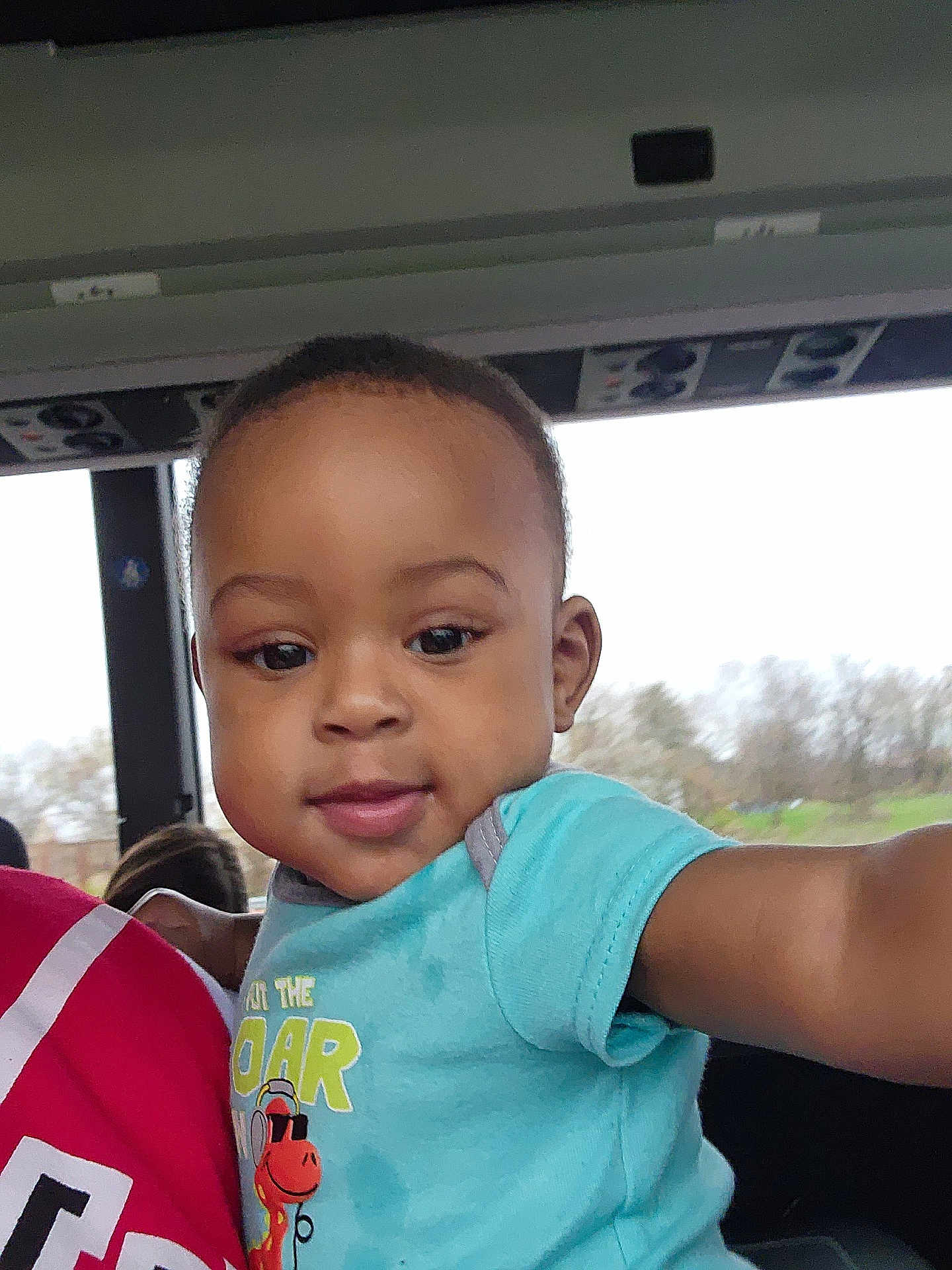 River joined the competition — help win amazing prizes! toddler, child, baby, face, smile, arm, shirt, giraffe, graphic, window, bus, vehicle, interior, person, expression, cute, young, portrait, reaching, blue_shirt