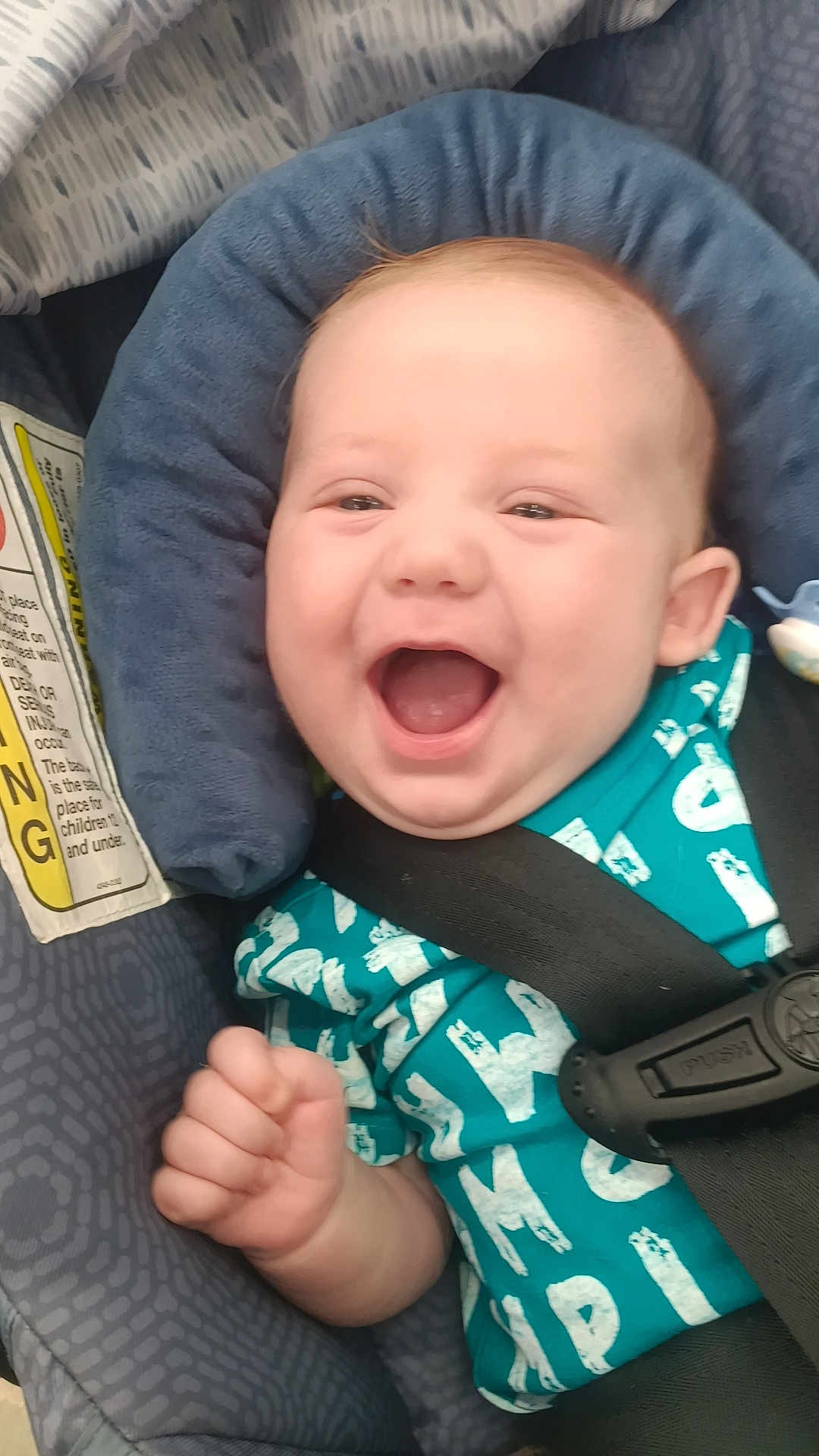 Weston is registered to the contest to win money with this photo: baby, child, car_seat, smiling, happy, infant, seatbelt, clothing, blue, padding, safety, cute, portrait, young, person, hand, face, indoor, seat, expression