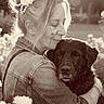 affection, animal, calm, casual_clothing, closeup, dog, embrace, flower, friendship, grass, happy, headpiece, love, nature, outdoor, pet, portrait, sepia, sunlight, woman