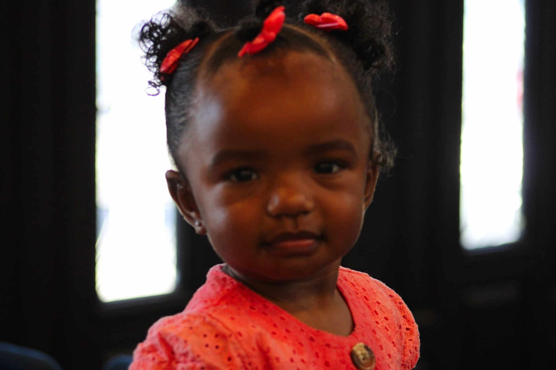 Harmony is registered to the contest to win money with this photo: toddler, child, girl, indoor, portrait, curly_hair, red_bows, coral_dress, button, face, expression, young, cute, person, childhood, fashion, hairstyle, skin_tone, looking_at_camera, soft_lighting