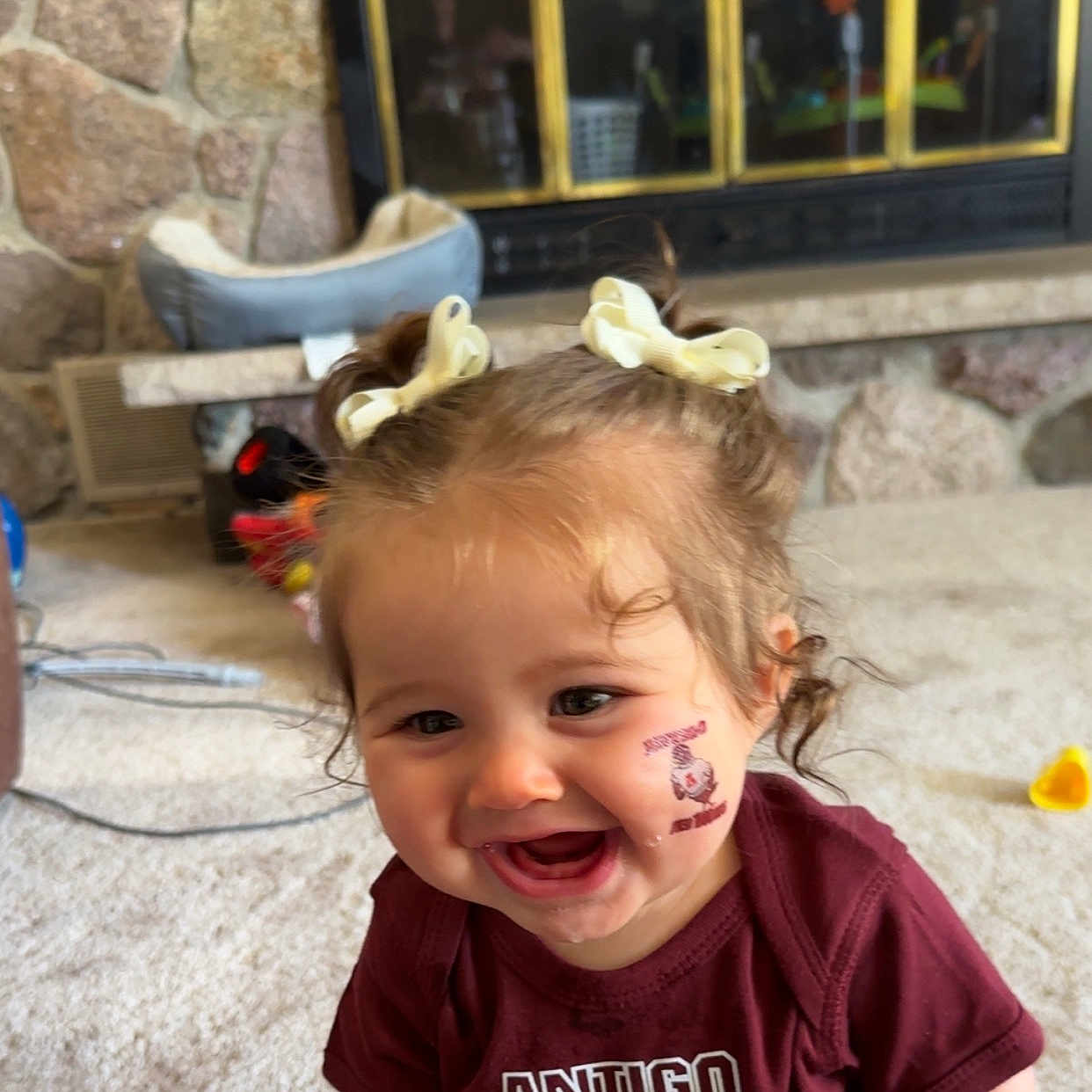 Kleo joined the competition — help win amazing prizes! bows, carpet, child, curly_hair, cute, drool, face, fireplace, happy, indoor, living_room, person, pigtails, shirt, smiling, stone_wall, temporary_tattoo, toddler, toys, young_child