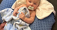 Jett is registered to the contest to win money with this photo: baby, blanket, pacifier, pillow, couch, infant, child, indoor, comfort, soft_texture, blue, brown, resting, person, portrait, relaxing, hand, face, head, cozy