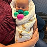 baby, infant, sleeping, pacifier, blanket, bunny_print, adult_hand, maroon_shirt, wrapped, cozy, indoor, couch, blue_furniture, cute, child, newborn, resting, soft_texture, colorful_eggs, peaceful