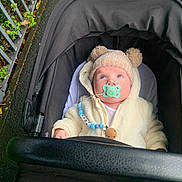 Roan joined the competition — help win amazing prizes! baby, stroller, pacifier, hat, coat, outdoor, sidewalk, fence, leaf, child, infant, blue_eyes, cute, warm_clothing, beads, black_stroller, person, hooded_jacket, winter, walking
