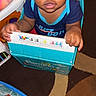 baby, blue_shirt, candid, cardboard_box, carpet, child, clothing, curious, expression, face, grip, home, indoor, pampers, patterned_floor, person, playtime, toddler, toy, young_child
