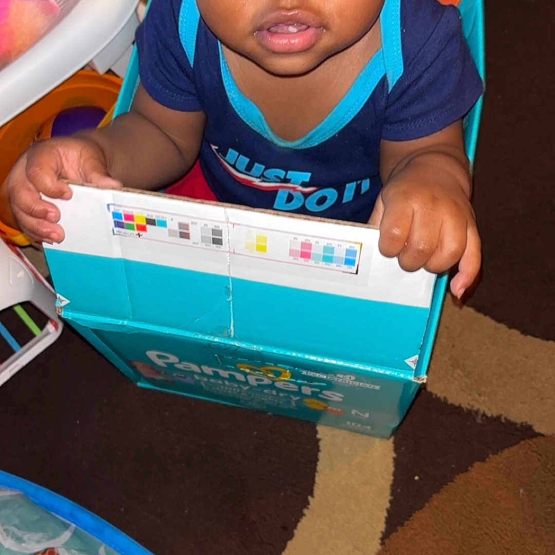 Daron Dee Rampey is registered to the contest to win money with this photo: baby, blue_shirt, candid, cardboard_box, carpet, child, clothing, curious, expression, face, grip, home, indoor, pampers, patterned_floor, person, playtime, toddler, toy, young_child