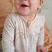 Elora is registered to the contest to win money with this photo: baby, child, smiling, onesie, sitting, bed, blanket, pacifier, happy, face, hair, indoor, young, infant, cute, person, portrait, cozy, clothing, skin