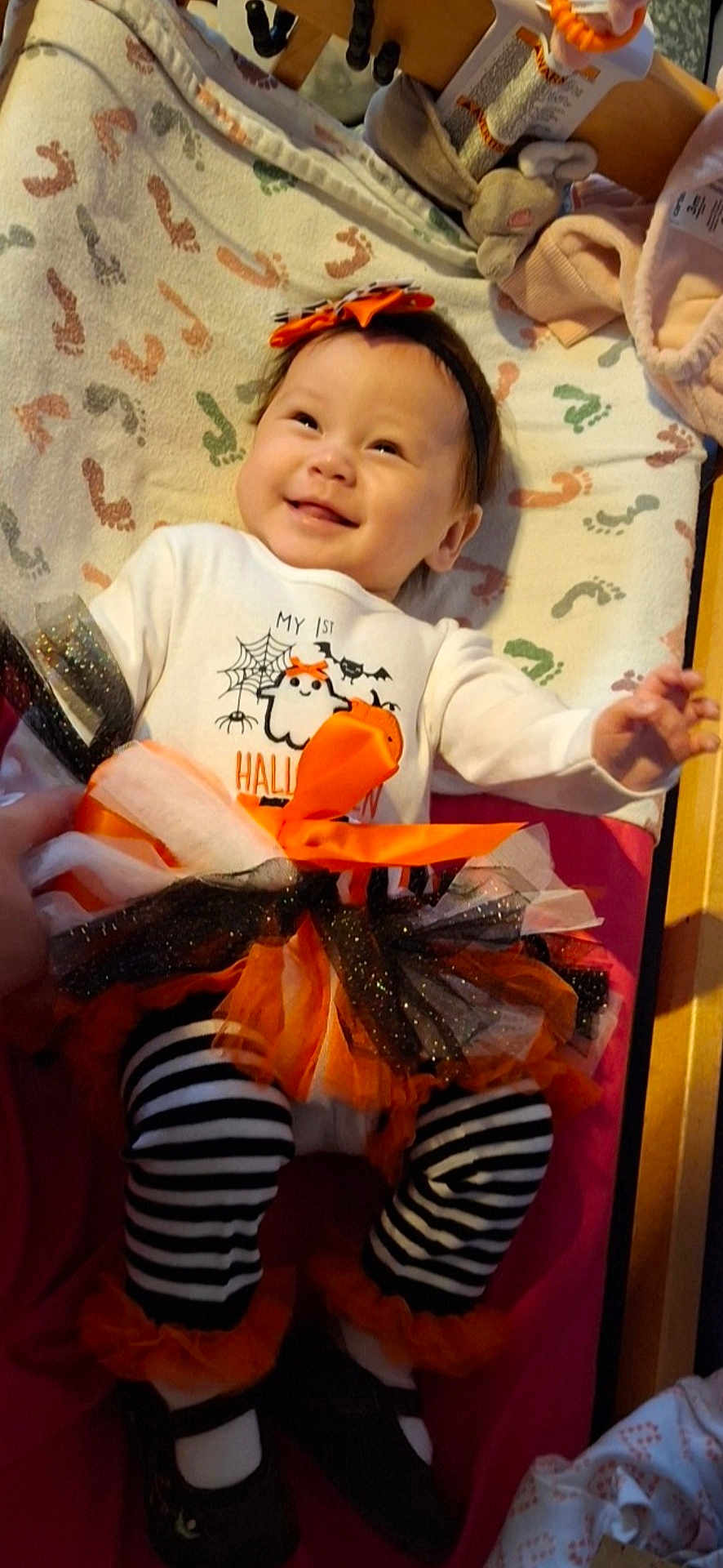 Elora is registered to the contest to win money with this photo: baby, child, smiling, halloween, tutu, striped_leggings, headband, blanket, footprints, costume, black_shoes, orange, white_shirt, cute, infant, happy, indoors, person, toddler, festive