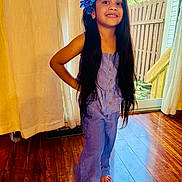 Ariah is registered to the contest to win money with this photo: child, girl, portrait, smiling, standing, indoors, window, sunlight, flower, hair_accessory, long_hair, purple_outfit, jumpsuit, barefoot, wooden_floor, curtain, backyard, fence, home, full_body