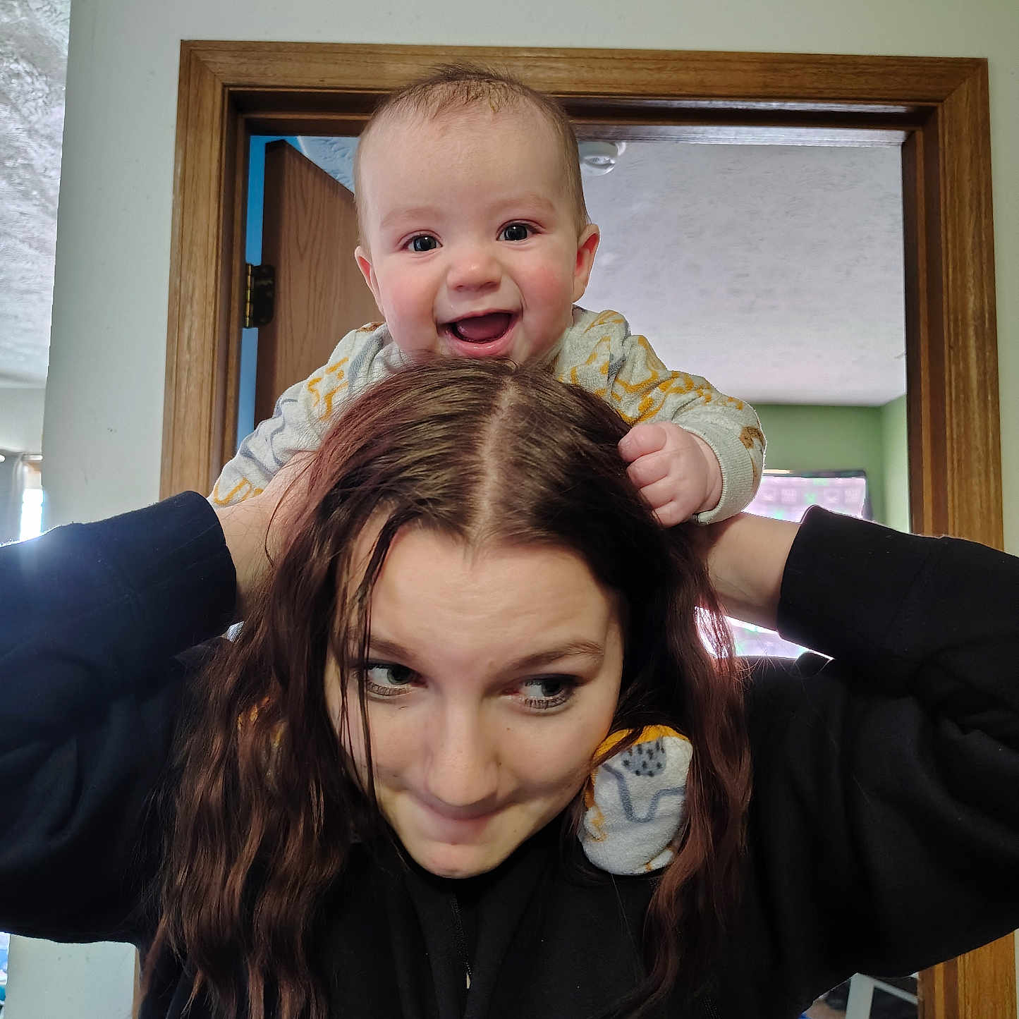 Jaythan is registered to the contest to win money with this photo: baby, black_sweatshirt, casual, child, cute, doorframe, expression, family, fun, hair, happy, home, indoor, interaction, person, playful, portrait, shoulders, smiling, woman