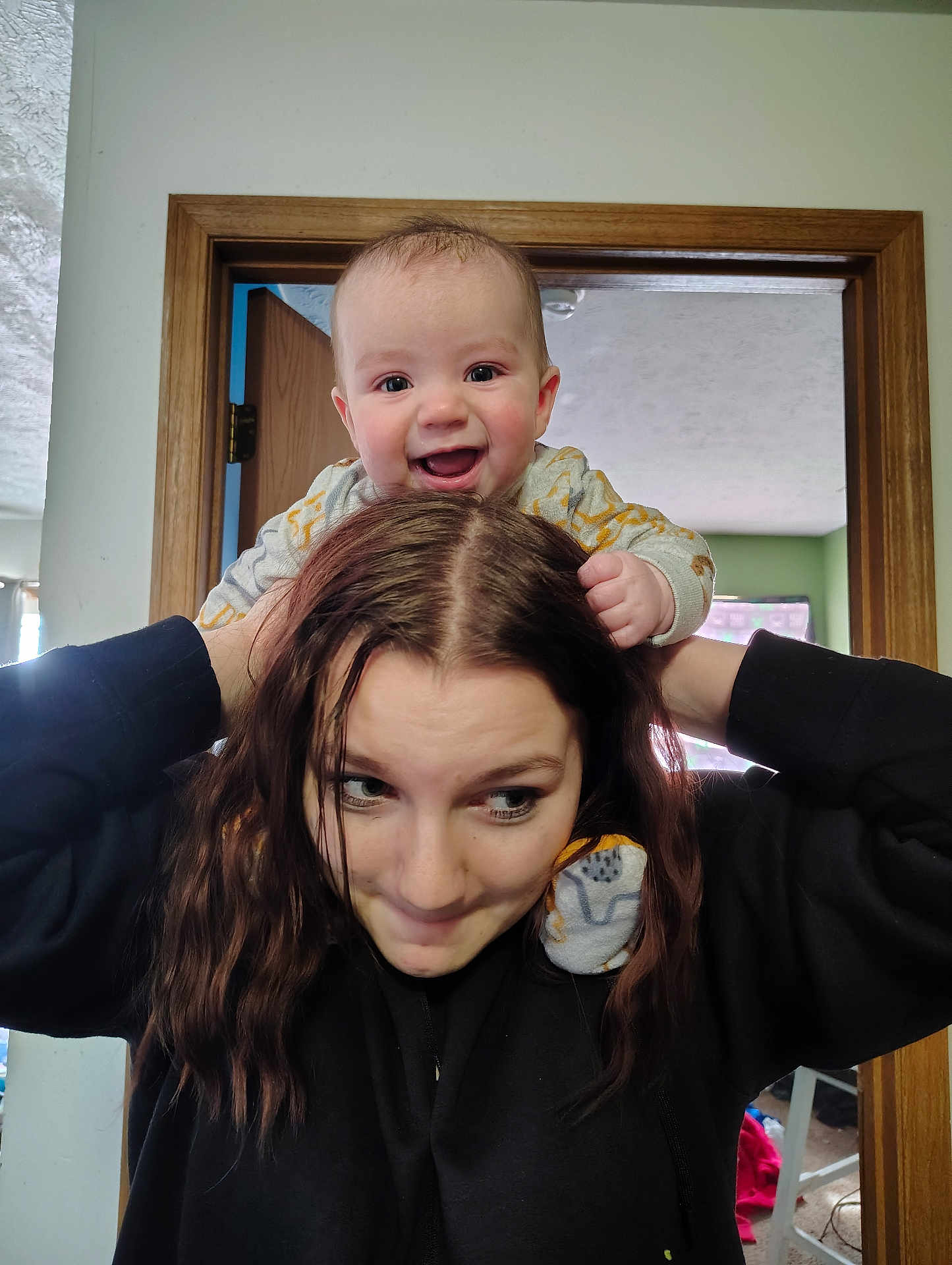 Jaythan is registered to the contest to win money with this photo: baby, child, woman, smiling, indoor, shoulders, playful, hair, happy, person, casual, black_sweatshirt, doorframe, home, portrait, cute, expression, fun, family, interaction
