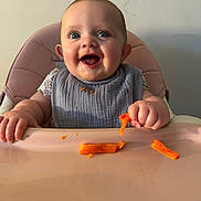 Willow joined the competition — help win amazing prizes! baby, high_chair, carrot, food, bib, happy, messy, child, eating, indoor, infant, smiling, face, hand, table, skin, clothing, person, cheerful, cute