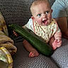 Willow is registered to the contest to win money with this photo: baby, blue_eyes, bib, couch, cozy, expression, face, food, green_vegetable, hand, heart_pattern, indoors, infant, joyful, person, plaid_blanket, sitting, skin, smiling, vegetable