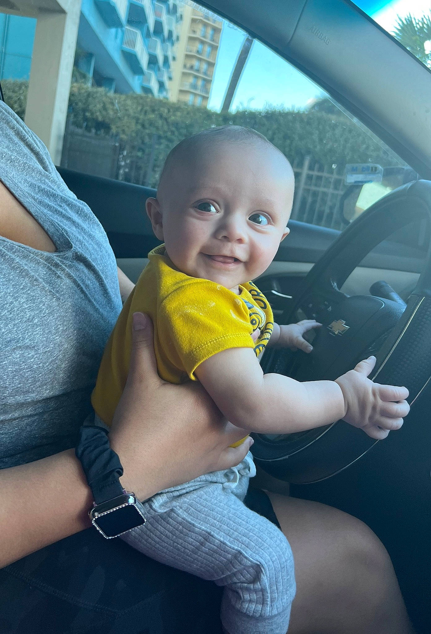 Bentley is registered to the contest to win money with this photo: arm, auto_part, automotive_exterior, baby, baby_toddler_clothing, car, car_seat, child, finger, happy, motor_vehicle, person, skin, sky, smile, steering_wheel, thigh, toddler, trunk, vehicle_door