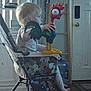 toddler, high_chair, toy, rubber_chicken, child, indoor, household, furniture, door, window, curtains, floor, footwear, clothing, person, face, hand, light, plastic, room