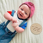 Beckham joined the competition — help win amazing prizes! baby, smiling, cap, denim_overalls, red, white, blue, infant, lying_down, hands, face, cute, happy, blanket, wooden_sign, celebration, holiday, portrait, closeup, indoors