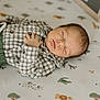 baby, sleeping, infant, plaid_shirt, green_pants, blanket, animal_print, face, peaceful, rest, lying_down, child, soft_lighting, indoor, portrait, cozy, cute, newborn, hand, relaxation