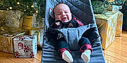 Tucker joined the competition — help win amazing prizes! baby, babybjorn, celebration, chair, child, christmas_lights, christmas_tree, cozy, cute, decorations, festive, gift_wrapping, holiday, home, indoors, infant, person, presents, smiling, wooden_floor