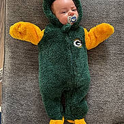 Tucker joined the competition — help win amazing prizes! baby, infant, onesie, green_bay_packers, pacifier, fuzzy_clothing, yellow, green, cushion, grey, indoor, flooring, wood_floor, child, cozy, cute, lying_down, face, head, person