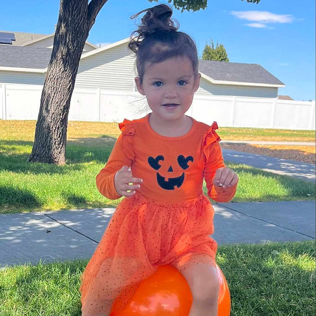 Aerith joined the competition — help win amazing prizes! bouncy_ball, child, cute, fence, girl, grass, happy, nature, orange_dress, outdoor, playful, portrait, pumpkin_face, shoes, sidewalk, smiling, suburb, summer, sunlight, tree