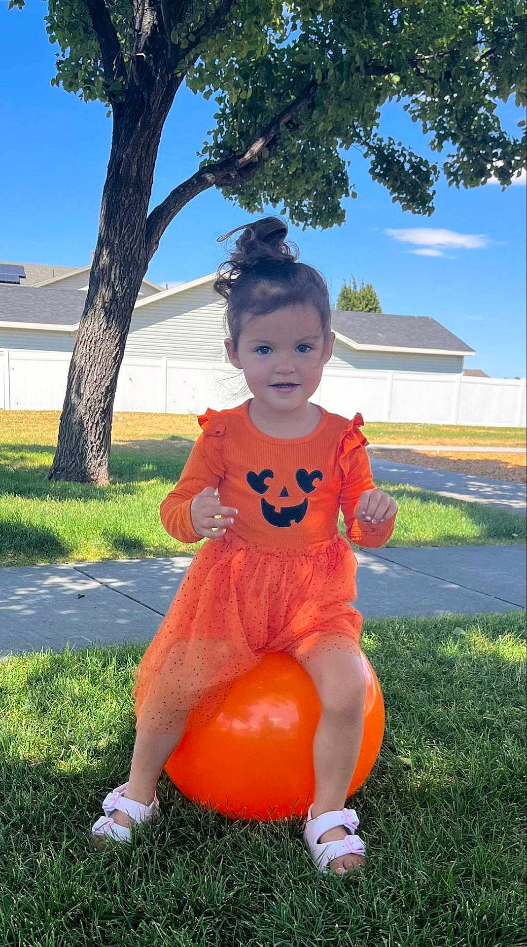 Aerith joined the competition — help win amazing prizes! child, girl, orange_dress, pumpkin_face, bouncy_ball, grass, tree, sunlight, shoes, sidewalk, fence, suburb, outdoor, happy, smiling, playful, summer, nature, portrait, cute