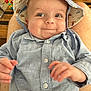 baby, child, smiling, hat, blue_shirt, person, indoor, toy, wooden_table, lap, happy, cute, face, eyes, skin, hand, button, clothing, infant, expression
