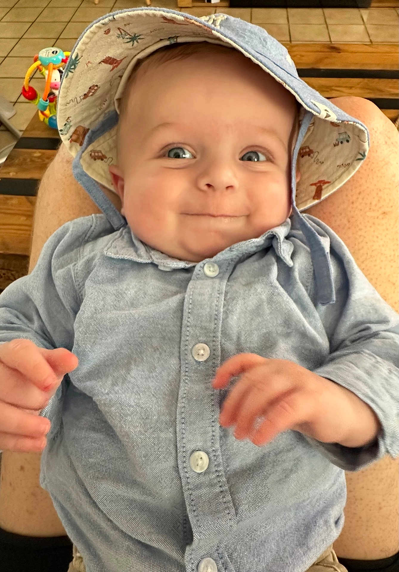 Milan participe au concours pour gagner de l'argent avec cette photo : baby, child, smiling, hat, blue_shirt, person, indoor, toy, wooden_table, lap, happy, cute, face, eyes, skin, hand, button, clothing, infant, expression