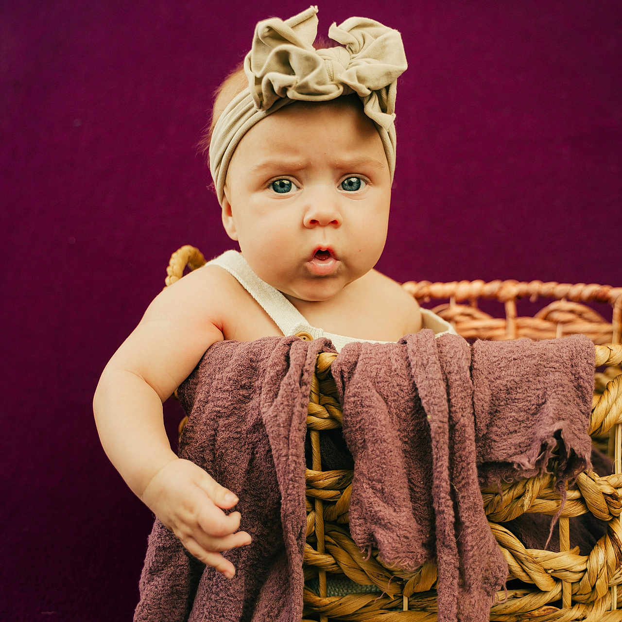 Lillie-Lynn is registered to the contest to win money with this photo: baby, basket, blanket, blue_eyes, bow, child, closeup, curious, cute, expression, hand, headband, indoors, infant, portrait, purple_background, sitting, soft_lighting, towel, woven