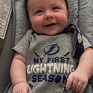 Jude joined the competition — help win amazing prizes! baby, smiling, infant, baby_seat, gray_shirt, text_on_clothing, patterned_fabric, hand, face, cute, child, indoor, soft_toy, happy, close_up, person, young_child, sitting, clothing, portrait