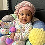 Iyla joined the competition — help win amazing prizes! baby, child, smiling, pink_bonnet, floral_pajamas, toy, colorful_cushion, indoor, cute, happy, sitting, infant, face, headwear, playful, comfort, bright_colors, portrait, young_child, joy