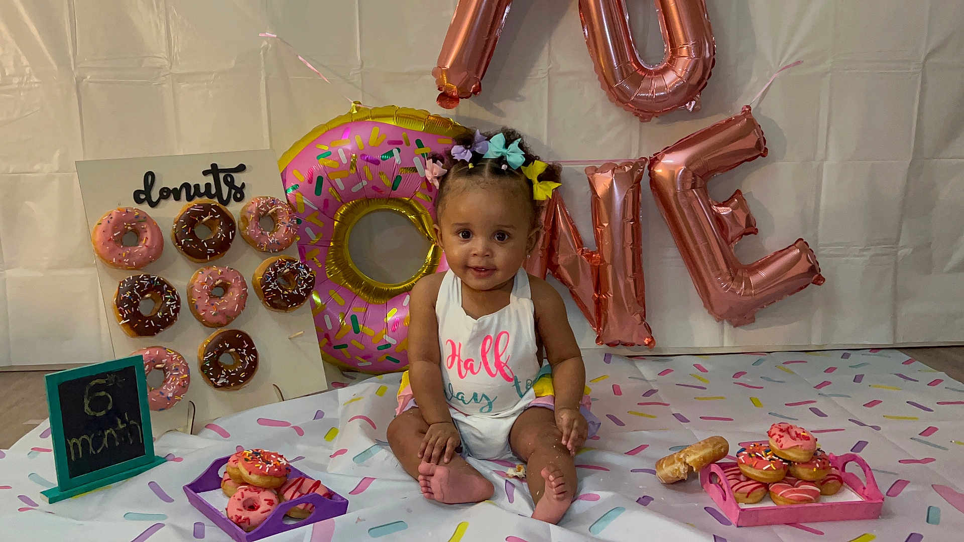 Iyla is registered to the contest to win money with this photo: baby, child, donuts, balloons, birthday, celebration, smiling, hair_bows, sitting, colorful, decorations, sprinkles, food, party, infant, festive, floor, cloth, portrait, cute