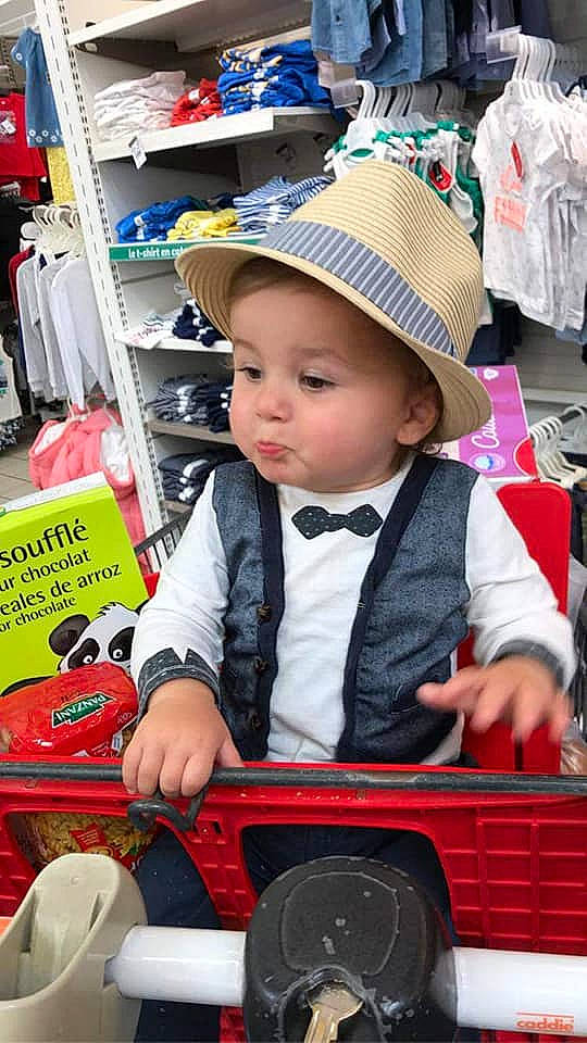 Ange participe au concours pour gagner de l'argent avec cette photo : baby, baby_toddler_clothing, cap, child, customer, event, fashion_accessory, fedora, fun, hat, headwear, market, marketplace, motor_vehicle, person, retail, shelf, shopping, sitting, sun_hat