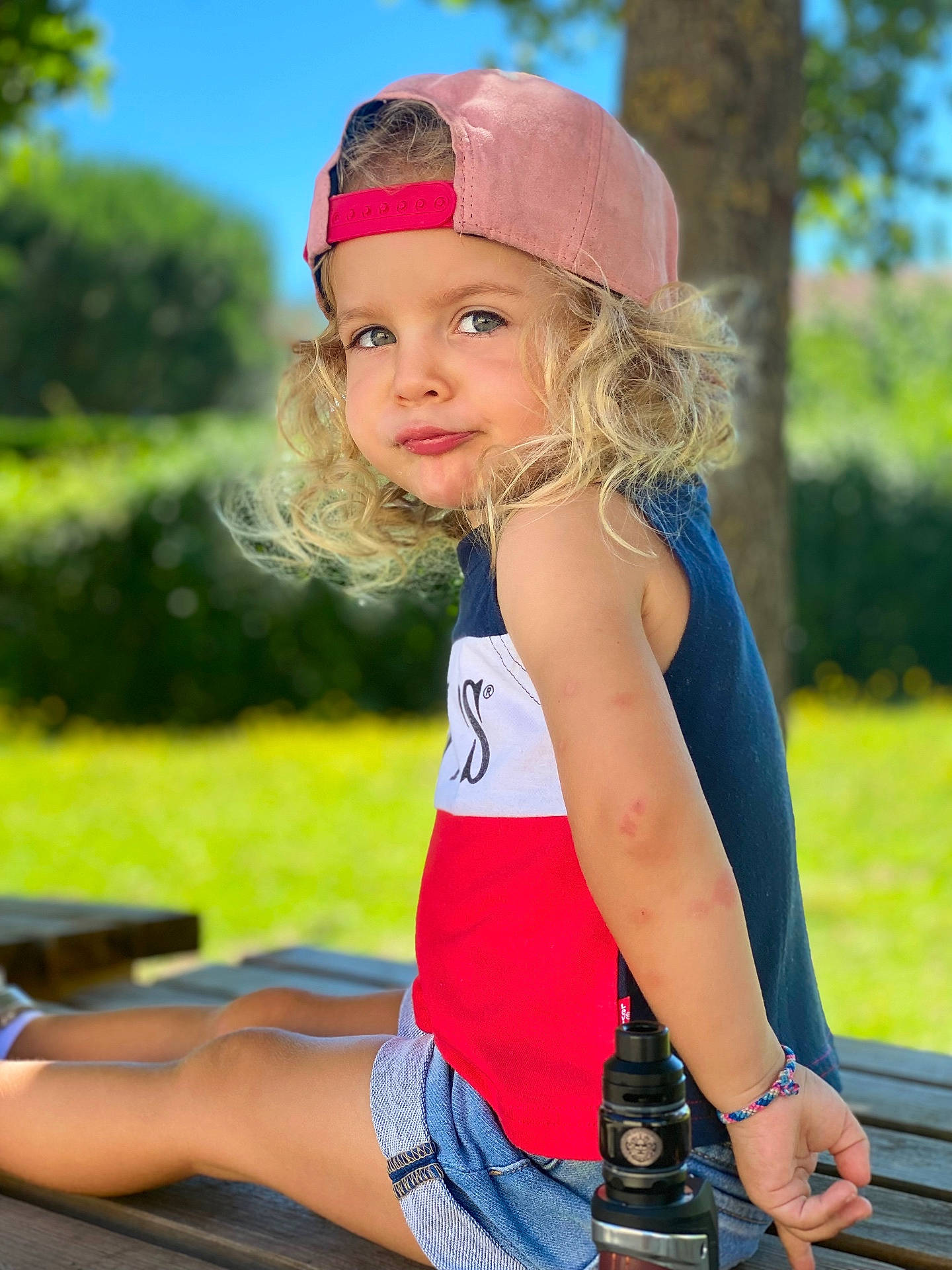 Thaïs participe au concours pour gagner de l'argent avec cette photo : baseballcap, bench, bodypart, cap, child, clothing, face, female, finger, furniture, girl, grass, hand, hat, head, person, photography, portrait, shorts, sitting