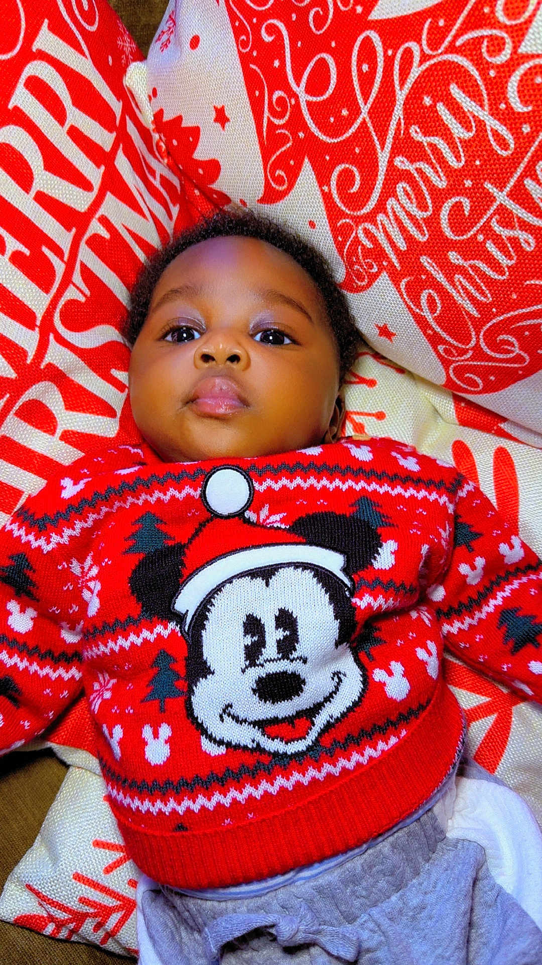 Ayomide is registered to the contest to win money with this photo: baby, child, mickey_mouse, red_sweater, christmas, holiday, pillow, face, portrait, cute, infant, smiling, lying_down, indoors, festive, clothing, young_child, holiday_season, cozy, bright_colors