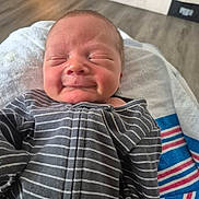 Leeland is registered to the contest to win money with this photo: baby, newborn, infant, child, portrait, smiling, sleeping, eyes_closed, striped_clothing, onesie, blanket, reclining, indoor, home, cozy, face, head, close_up, colorful_blanket, photography