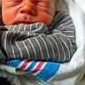 Leeland is registered to the contest to win money with this photo: newborn, baby, infant, child, sleeping, scrunching, face, portrait, bundled, blanket, swaddled, striped_clothing, gray, blue, white, red, cozy, indoors, close_up, photography