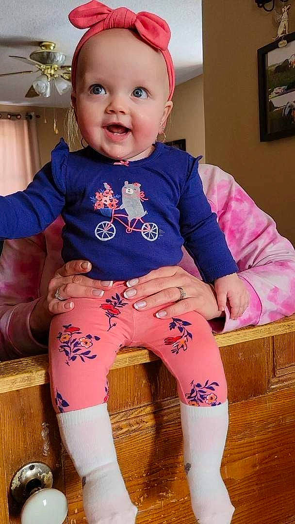 Haley is registered to the contest to win money with this photo: baby, baby_toddler_clothing, cheek, child, fun, happy, human_leg, knee, magenta, pattern, person, picture_frame, pink, purple, sitting, skin, sleeve, smile, t_shirt, thigh